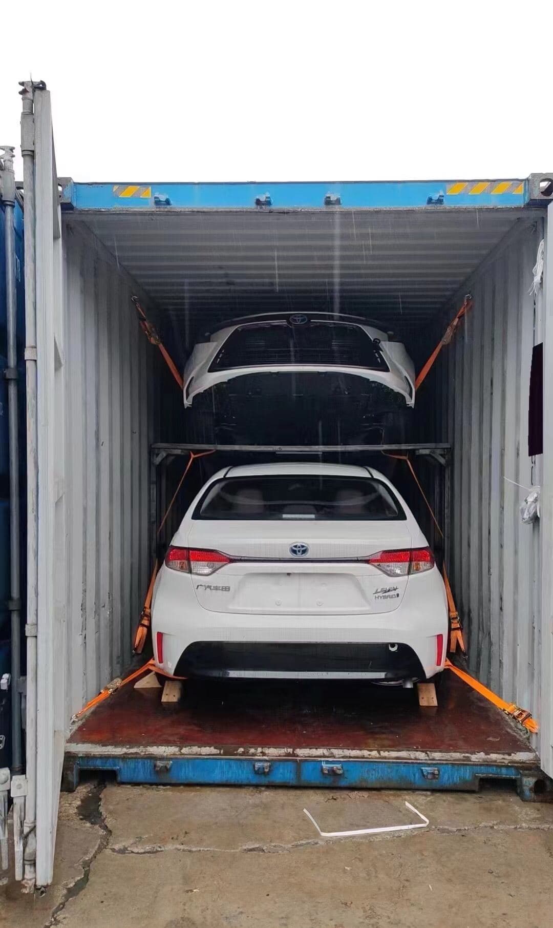 Two sedans loaded on a two-tier rack inside a 40-foot container